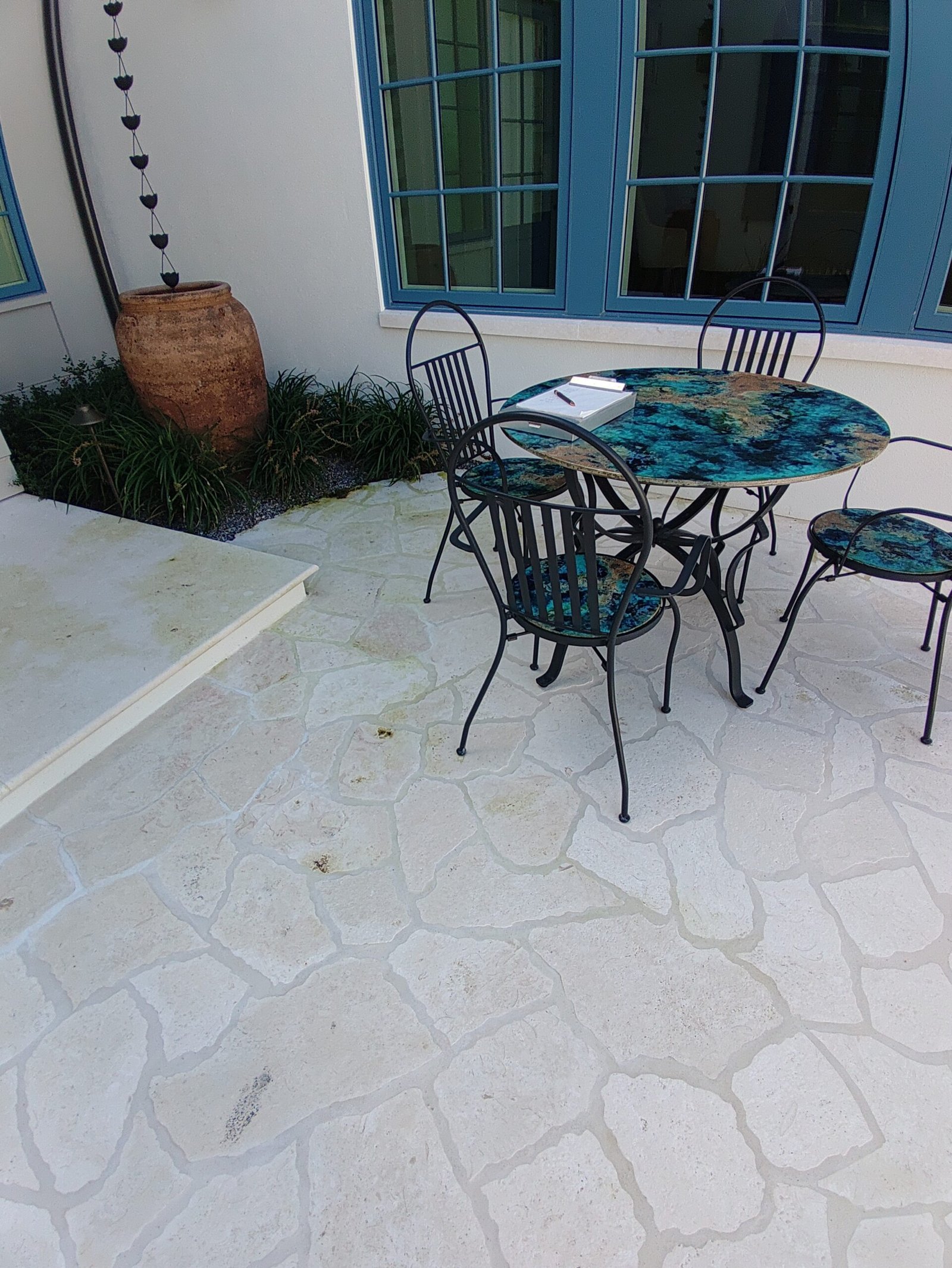Pale patterned patio tiles beside a blue-framed window and a metal outdoor table